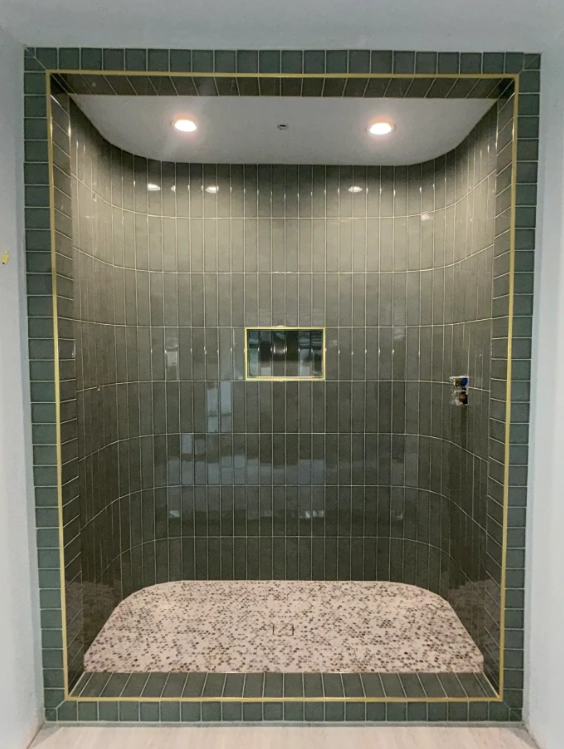 Bold dark green subway tile shower with gold trim in a Kyle bathroom