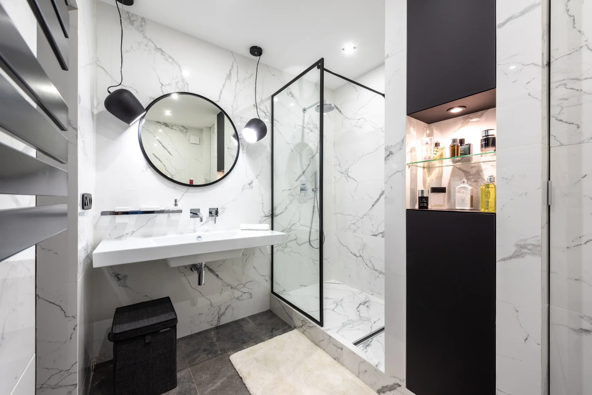 Elegant white marble tile bathroom with round mirror, floating vanity, and glass shower